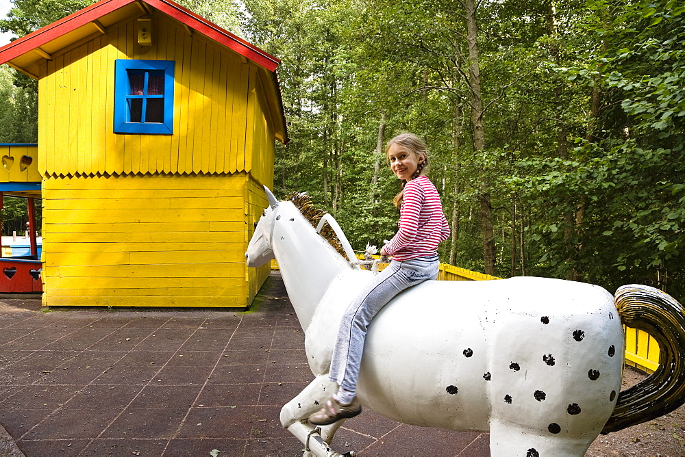 Girl sitting on a wooden horse, Astrid Lindgren Vaerld, Astrid Lindgren World, Vimmerby, Smaland, South Sweden, Europe